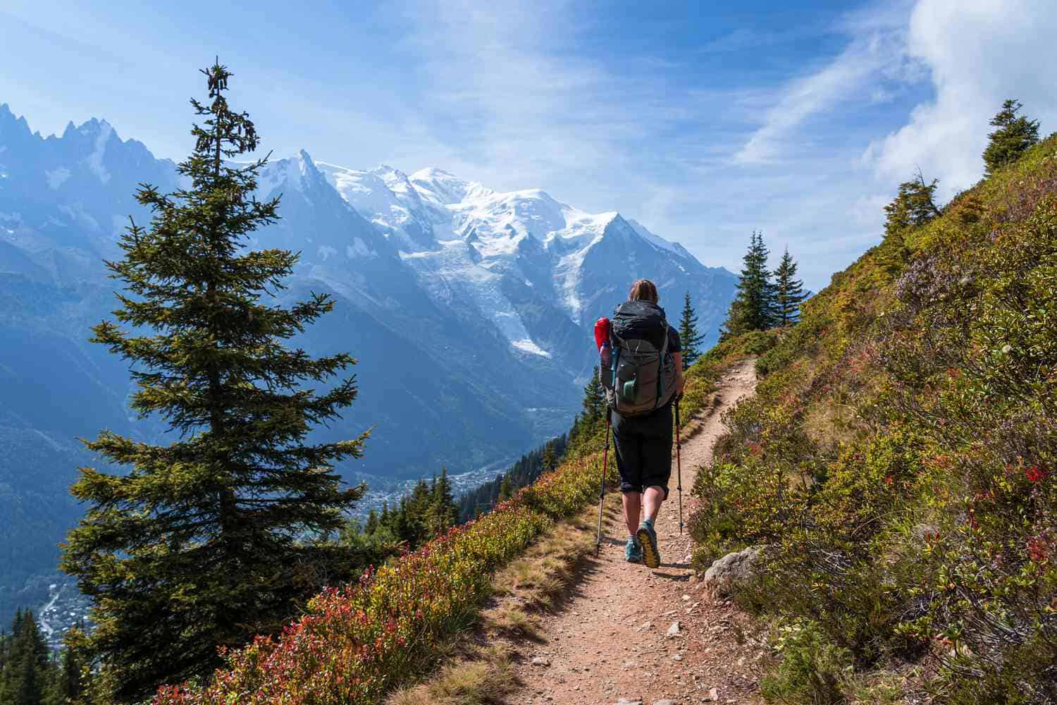 A hiker walking on a scenic mountain trail with snow-capped peaks