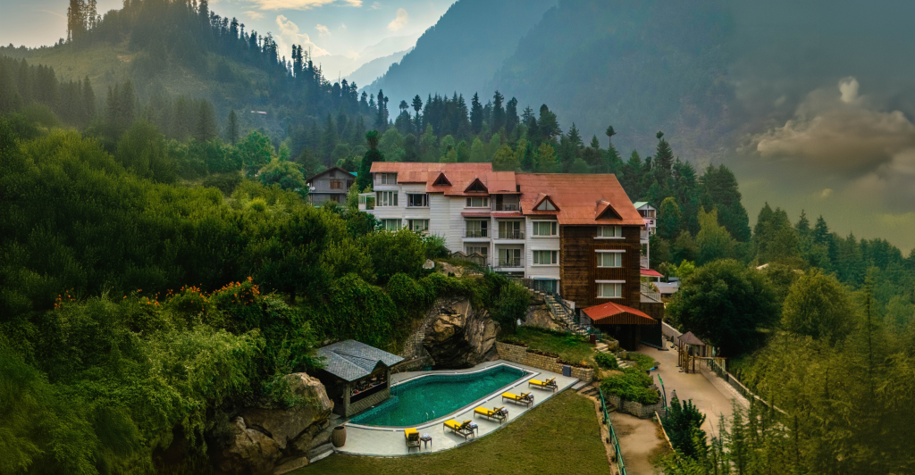 A scenic view of the resort nestled in the mountains with a pool and lush greenery | Bookmark Resorts, Manali