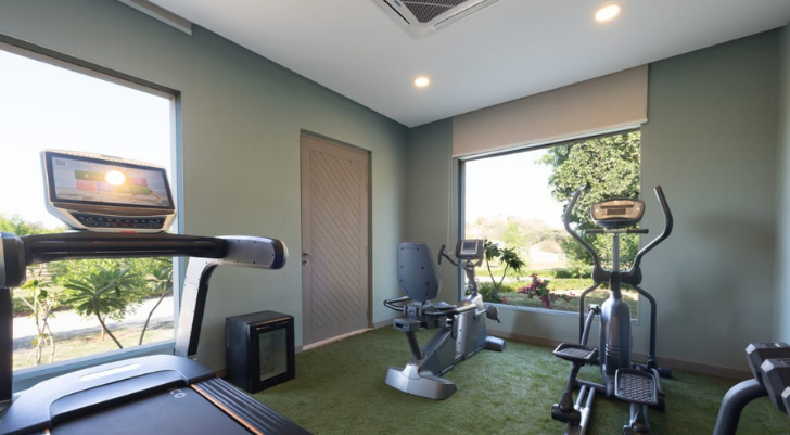 Gym Small private gym with a treadmill, stationary bike, and elliptical machine, plus large windows showing outdoor greenery.