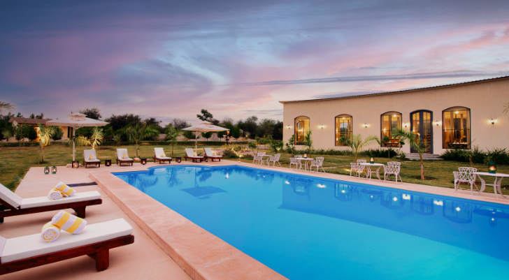 Swimming Pool Outdoor luxury resort pool at dusk: a rectangular blue pool, white loungers with towels, umbrellas, and a light building with arched windows.