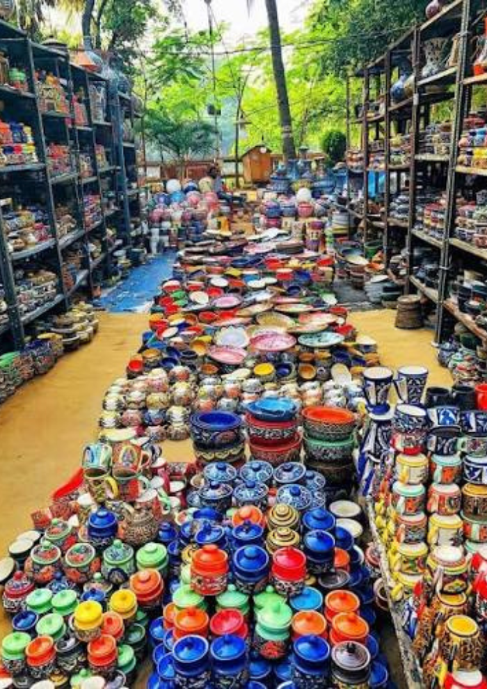 Outdoor market stall filled with colorful ceramic bowls, pots, and mugs arranged in rows on the ground and shelves along the sides.