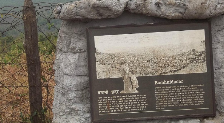 Informational plaque on a stone pillar with a black-and-white photo of a man and a child and multilingual text about a local site.