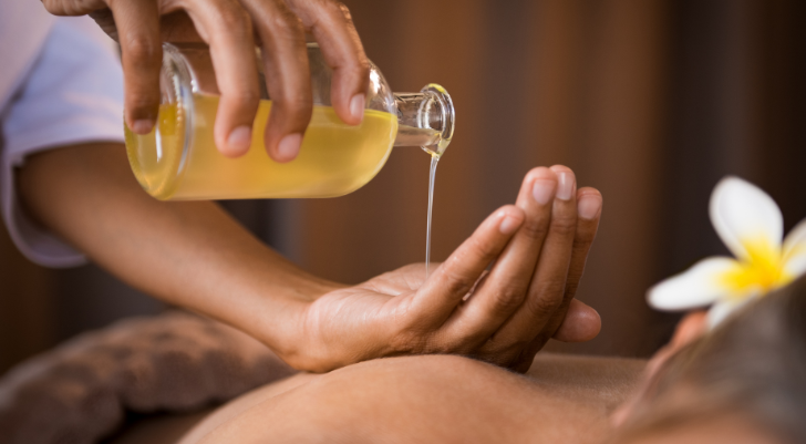 Spa treatment: pouring warm oil onto a person's back during a massage session.