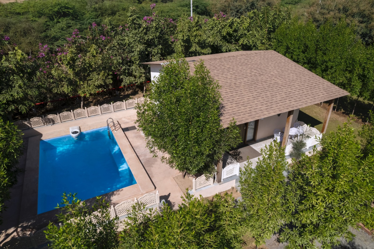 Aerial view of a beige-roofed villa with a rectangular blue pool, white fencing, and surrounding trees.