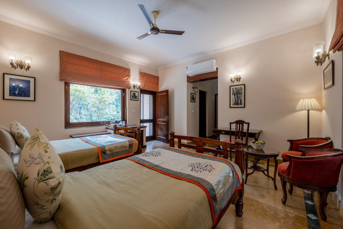 Hotel room with two single beds, wooden headboards, and a window showing trees outside.