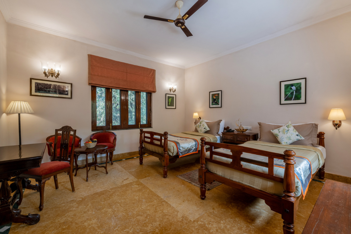 Twin-bed hotel room with dark wood frames, bedside lamps, and a seating area by the window