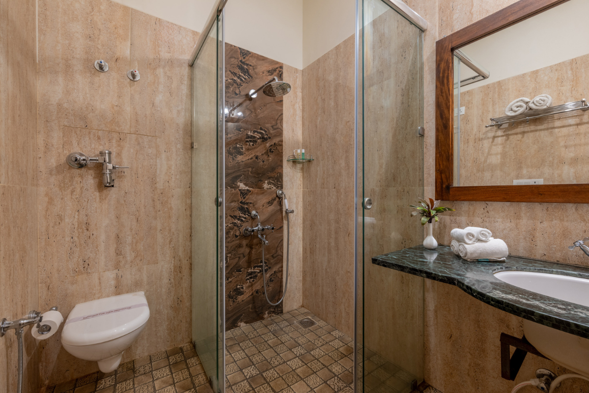 Hotel-style bathroom with a glass-enclosed shower, wall-mounted toilet, and marble countertop with folded towels beneath a wooden-framed mirror