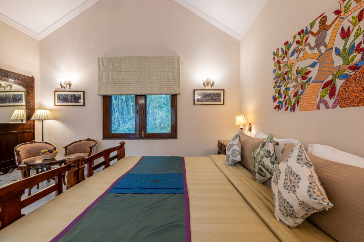 Hotel room with a large bed, colorful wall art, and a seating area by a window; warm lamps and tropical-patterned cushions create a cozy ambiance.