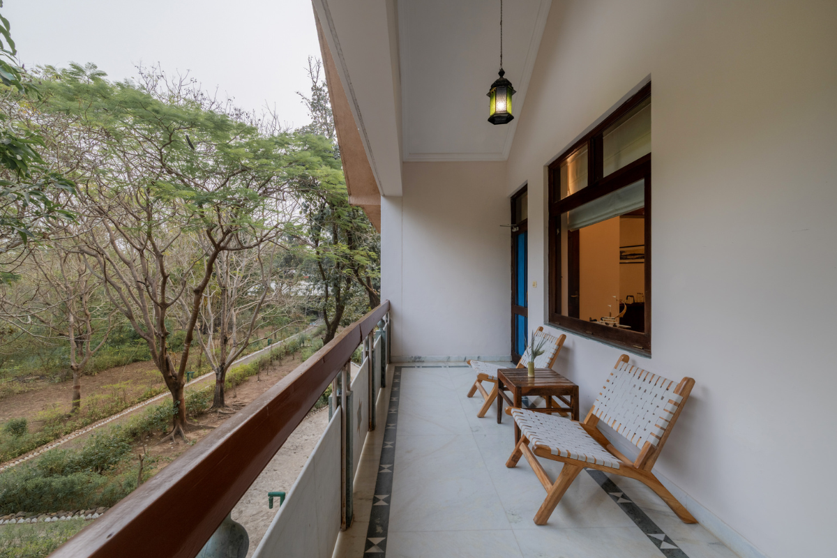 Balcony seating area with two woven chairs and a small wooden table overlooking a garden with trees and greenery.
