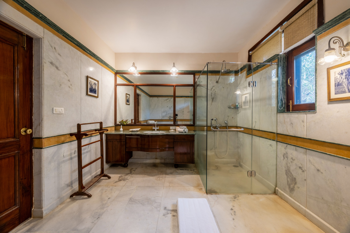 Luxurious marble bathroom with a glass shower, wooden vanity, large mirror, and framed photos