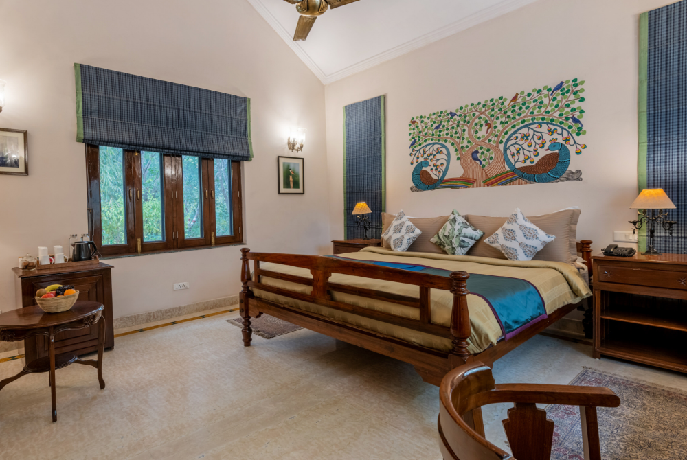 Hotel-style bedroom with a large wooden bed, beige bedding, and a colorful tree-and-peacock mural above the headboard.