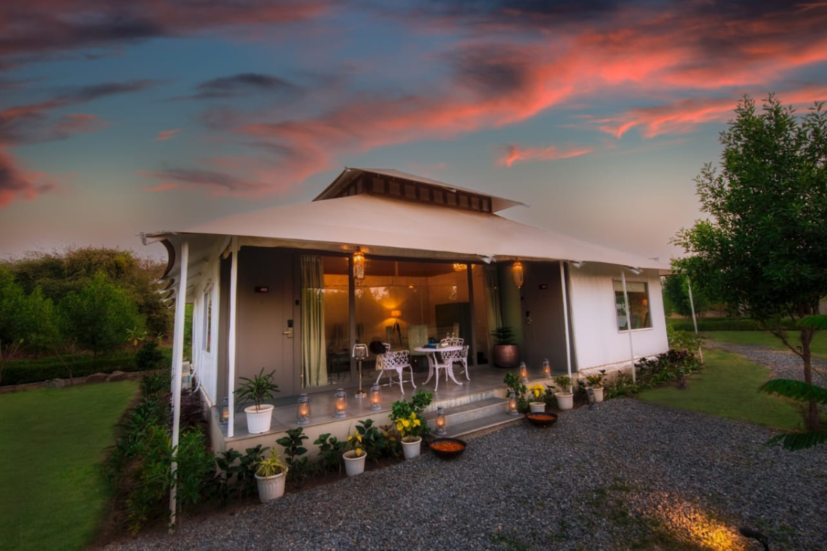 Cozy white house with a covered porch, string lanterns, and potted plants at sunset