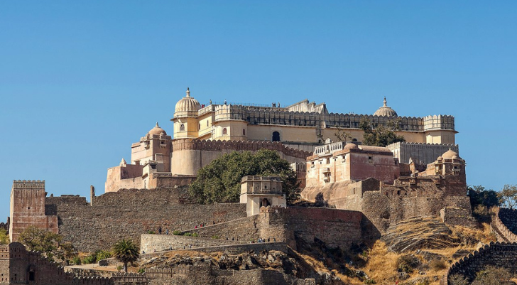 Amber Fort perched on a rocky hill with orange sandstone walls and domed towers against a clear blue sky.