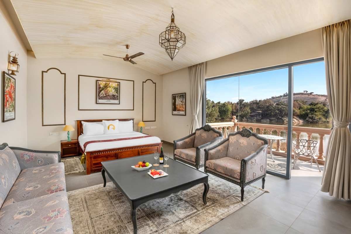 Luxurious hotel room with a king bed, seating area, and a sliding glass door to a balcony overlooking hills.