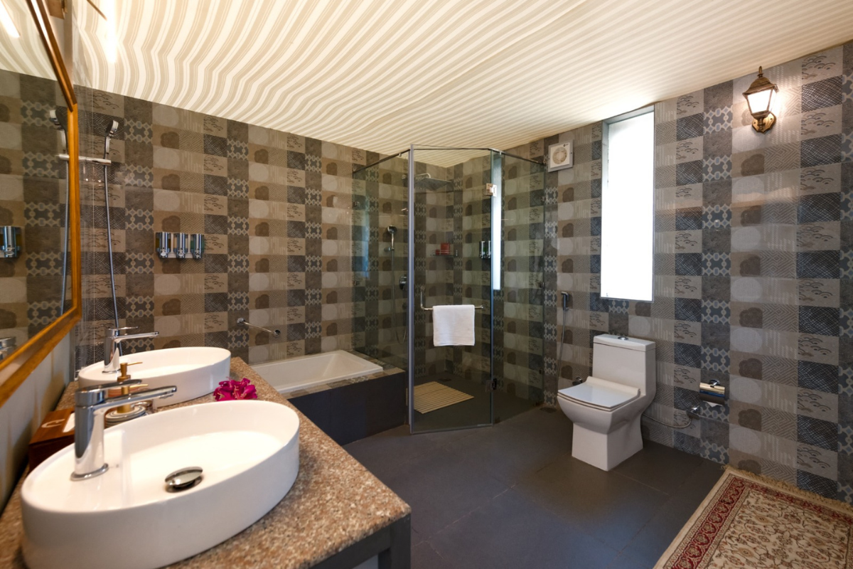 Bathroom with two oval sinks on a granite counter, a mirror, and patterned tile walls.