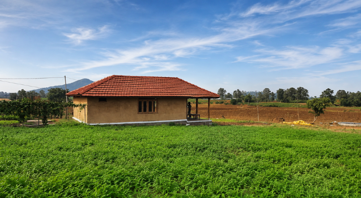 Single-story beige house with a red tile roof in green farmland under a blue sky (rural setting)