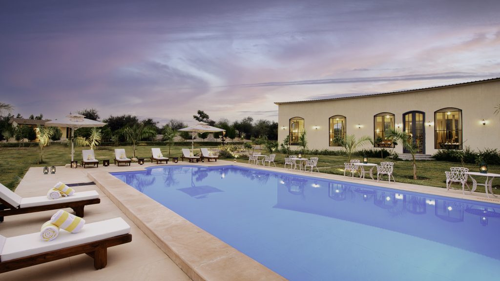 Luxury hotel pool area at dusk with white lounge chairs, umbrellas, and a beige building with arched windows