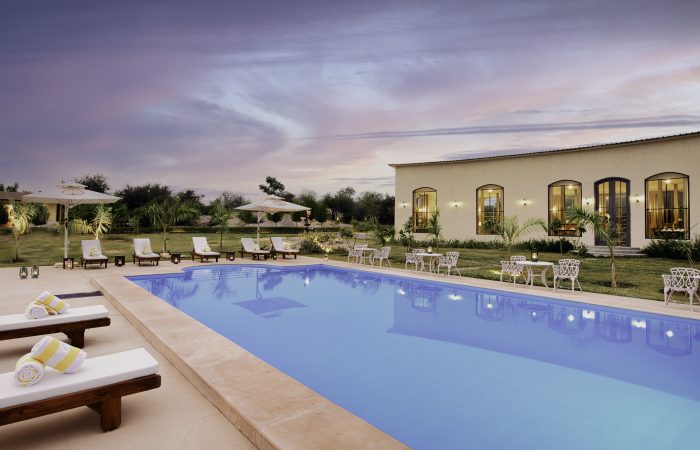 Pool1 Luxury hotel pool area at dusk with white lounge chairs, umbrellas, and a beige building with arched windows