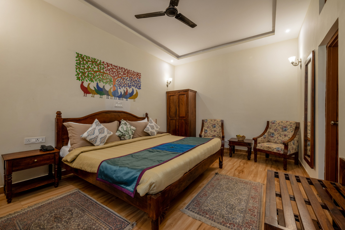 Cozy hotel bedroom with a wooden bed, beige bedding, colorful quilt, side tables, and a tall wooden wardrobe.