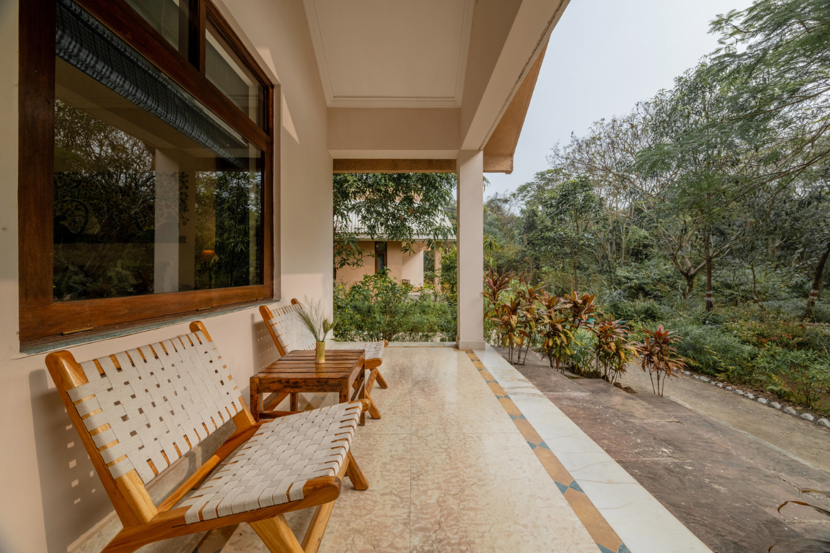 Wooden outdoor chairs and a small table on a covered veranda, facing a garden.