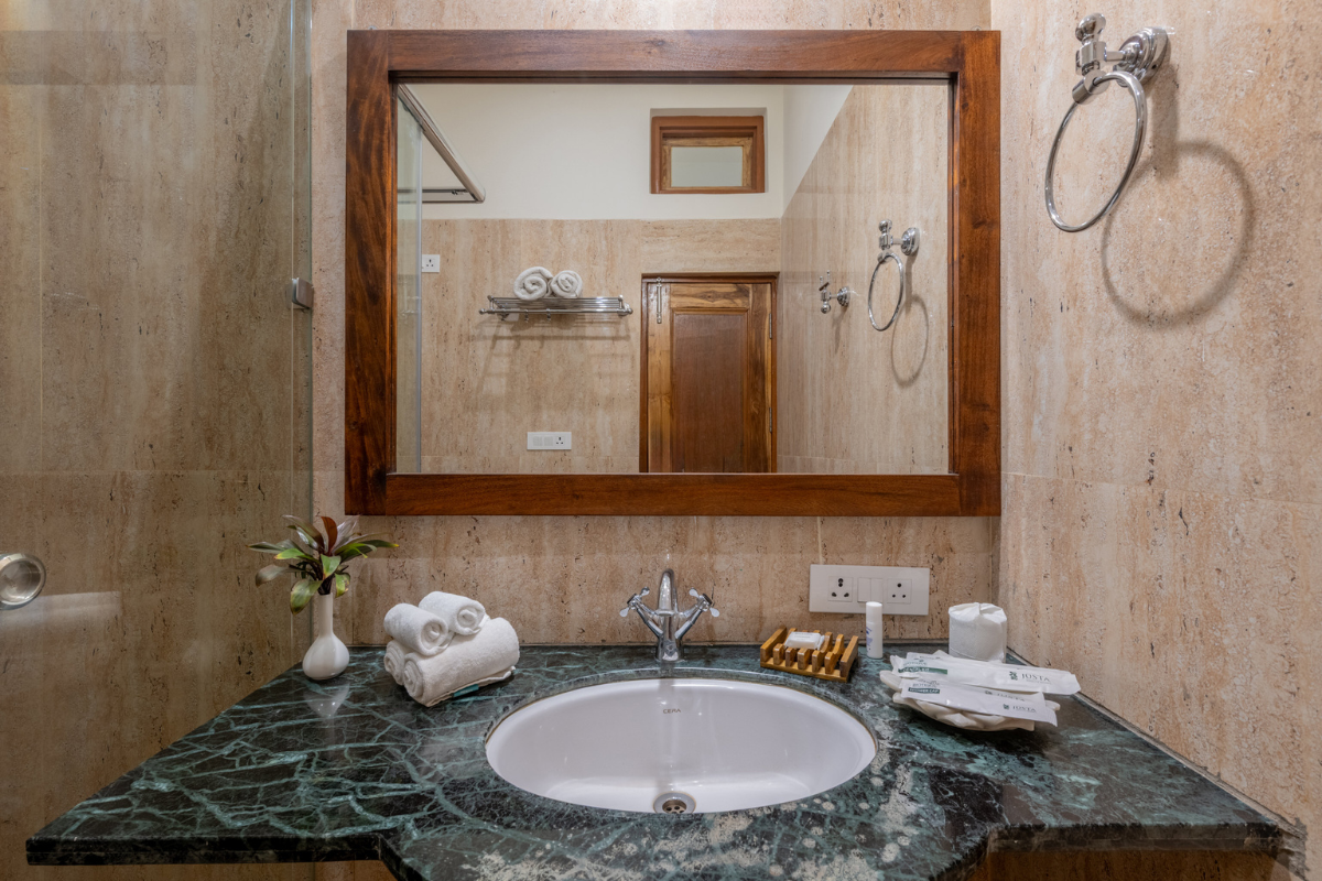 Bathroom vanity with dark green marble countertop, white sink, and large wooden-framed mirror; towels and toiletries on counter.