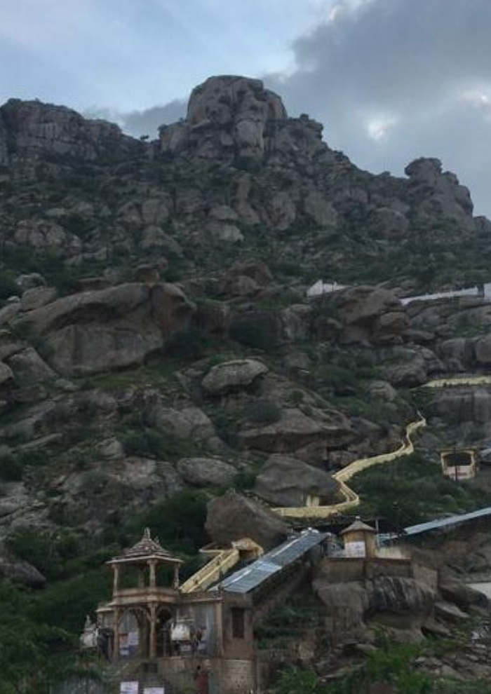 TEMPLE & SPIRITUAL CIRCUIT Rugged rocky hillside with a winding yellow path leading to a small temple at the base among large boulders.