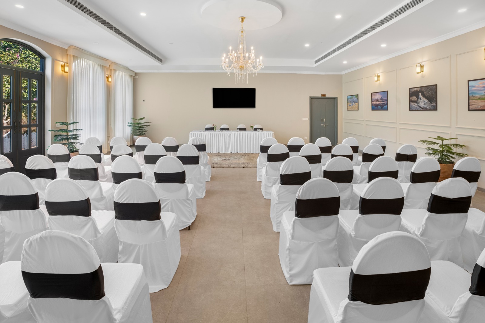 Banquet hall prepared for a formal event with rows of white chair covers and black sashes facing a head table under a chandelier.